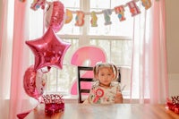 a little girl sitting at a table with balloons in front of her